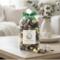 Irish Twins 'Cotton Fields' potpourri on wooden table. Cozy living room background with white sofa and cotton flowers. Fresh home fragrance.